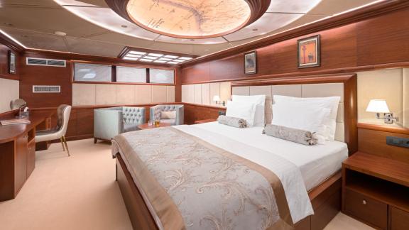 Eine luxuriöse Masterkabine mit Kingsize Bett, Sitzecke, Schreibtisch und eine dekorative Designer Lampe.